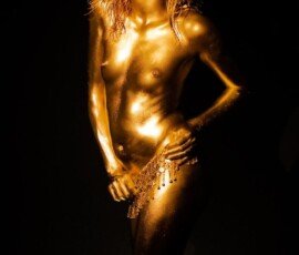 Stunning gold body paint photo featuring metallic makeup and jewelry. Artistic body art highlighting metallic skin tone against black background. Golden body paint art with a glittering jewelry necklace. Creative and elegant body art photography showcasing metallic skin.