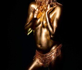 Shimmering gold body paint and jewelry on a dancing woman create a striking artistic image. Glamorous woman with body painted in metallic gold, wearing a belly dance-inspired coin belt, surrounded by dark background.