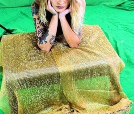 Young woman with blonde hair and tattoos posing with cowboy hat on green screen for photography project. Vrouw met cowboy hat leaning on a shiny gold table against green screen background.