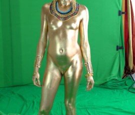Gold body paint human model wearing Egyptian-themed jewelry and accessories in front of green screen. Gold painted human model with Egyptian accessories against green screen background.