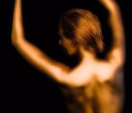 Stylish portrait of a woman with short red hair and graceful arm pose in dramatic lighting. Elegant woman with short red hair posing with arms raised against a black background.
