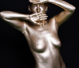 Elegant body art photography featuring a nude model with metallic gold body paint and creative hand placement. Glamour woman with body paint and artistic pose, studio shot against black background.