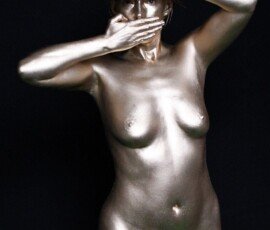 A stunning artistic nude portrait featuring metallic gold body art and expressive pose. Glamorous woman with metallic gold body paint, posing creatively against a black background.