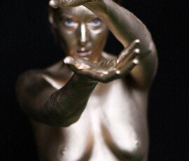A nude woman painted in gold with outstretched hands on a dark background, capturing artistic body art and modern portrait photography. Gold painted nude woman with outstretched hands, artistic photography, dark background, metallic body art, modern creative portrait.