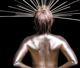 A person with metallic body paint poses against a black background, with hands on hips and an artistic halo of metal rods around their head. Shiny metallic body paint on a person's back with a radiant halo of metal rods, showcasing artistic photography.