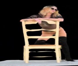 Fashion portrait of a woman posing on a chair for a modern photography shoot. Woman sitting on a wooden chair with a black background, wearing sunglasses and stylish clothing.